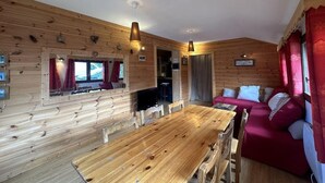 L’intérieur d’un chalet chaleureux, avec une table à manger en bois, un canapé rouge et un téléviseur.