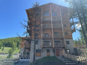 Un edificio de madera de varios pisos con balcones, una entrada de piedra y una vista despejada del bosque circundante.