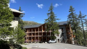 Un chalet avec une façade en bois, plusieurs balcons et un espace de stationnement.