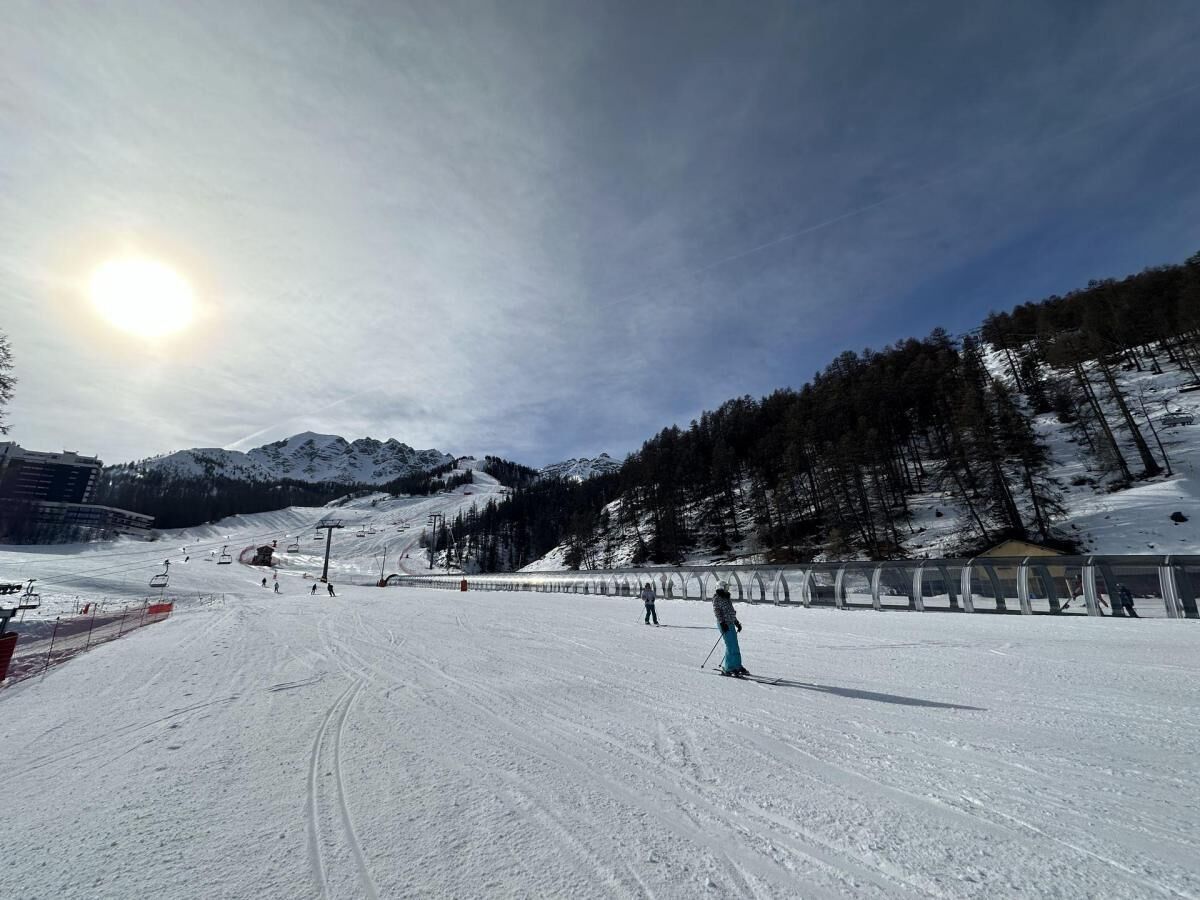 Une piste de ski enneigée, avec des skieurs, un télésiège et une montagne en arrière-plan.