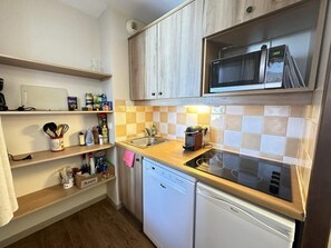 A compact kitchen with wooden cabinets, a microwave, a dishwasher, and a tiled backsplash.