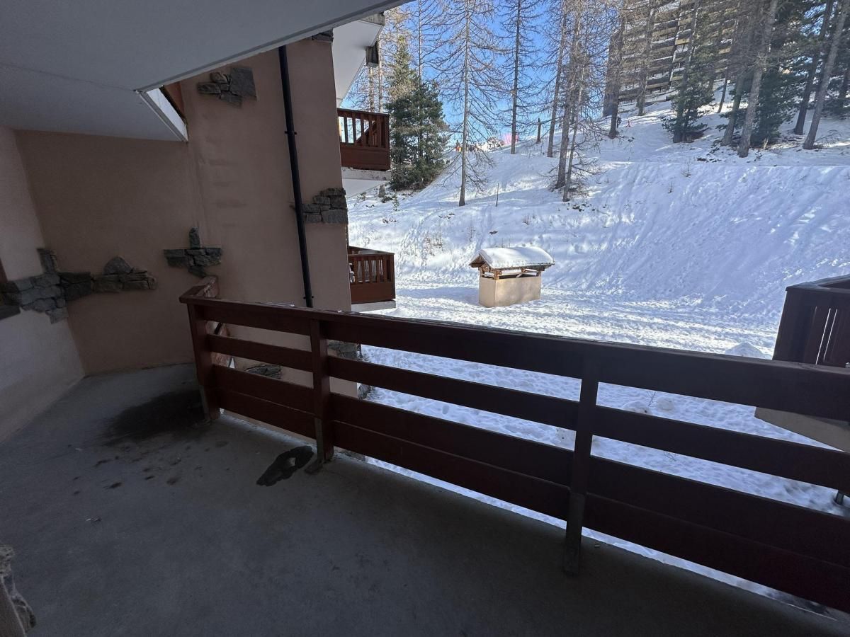A balcony with a wooden railing overlooking a snowy landscape with trees and a building in the background.