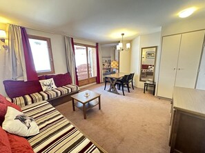 Een woonkamer met een bank, een salontafel, een eethoek met stoelen en een keuken op de achtergrond.