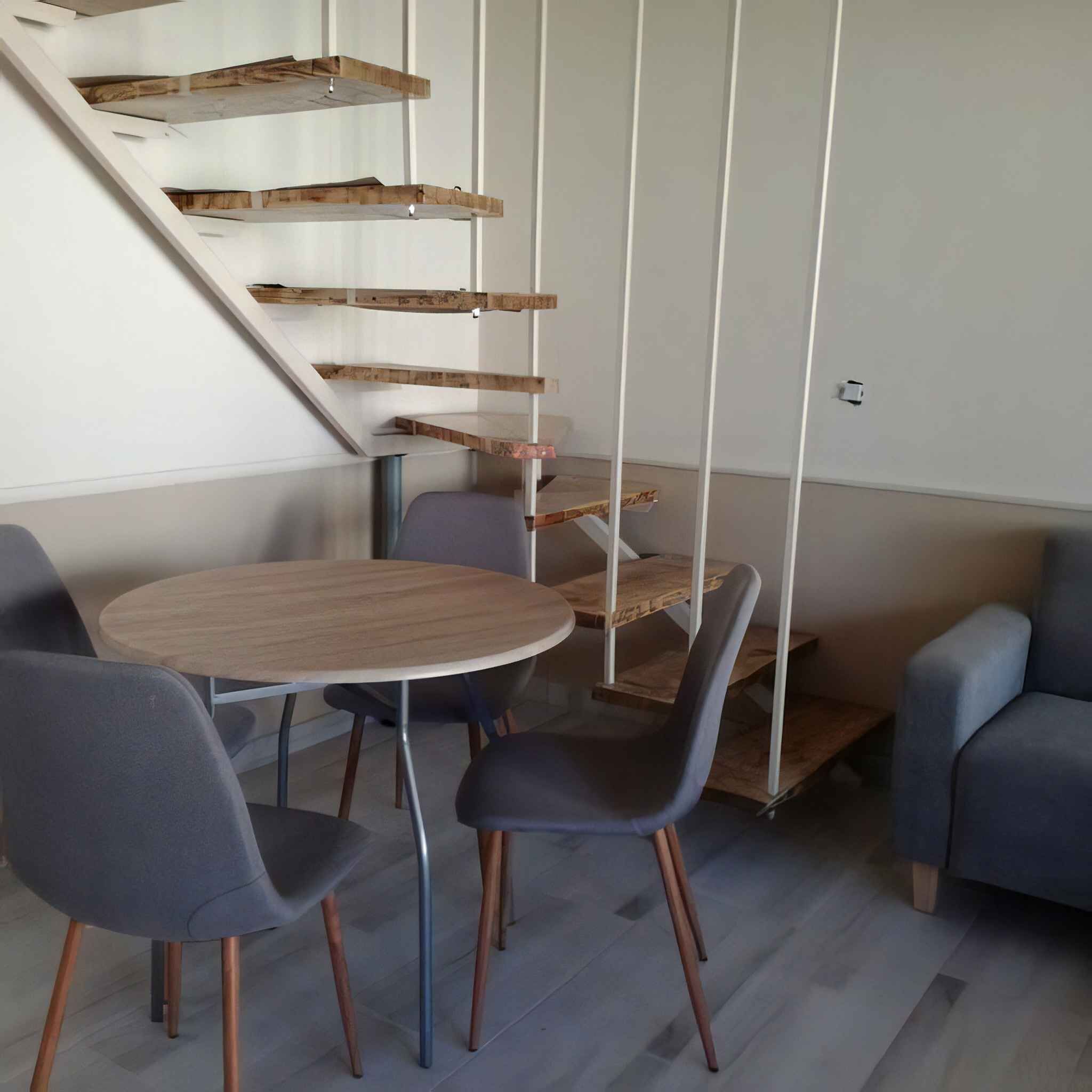 Een modern interieur met een spiltrap, een ronde houten tafel en twee grijze stoelen.