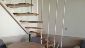 Et moderne interiør med en spiraltrappe, et rundt træbord og to grå stole.