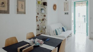 A dining area with a table set for four, a sofa with cushions, and a wall with framed artwork and a decorative plate. - Nina Delle Palme in Monopoli (Monopoli)