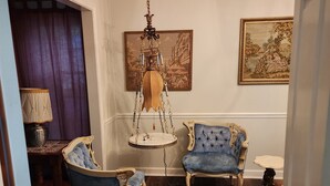 A room with two blue armchairs, a hanging chandelier, and two paintings on the walls.