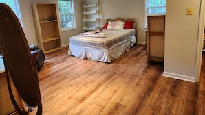 A bedroom with a bed, wooden flooring, built-in shelving, and windows.