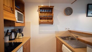 Una cocina compacta con armarios de madera, un microondas, una cafetera y un lavamanos.
