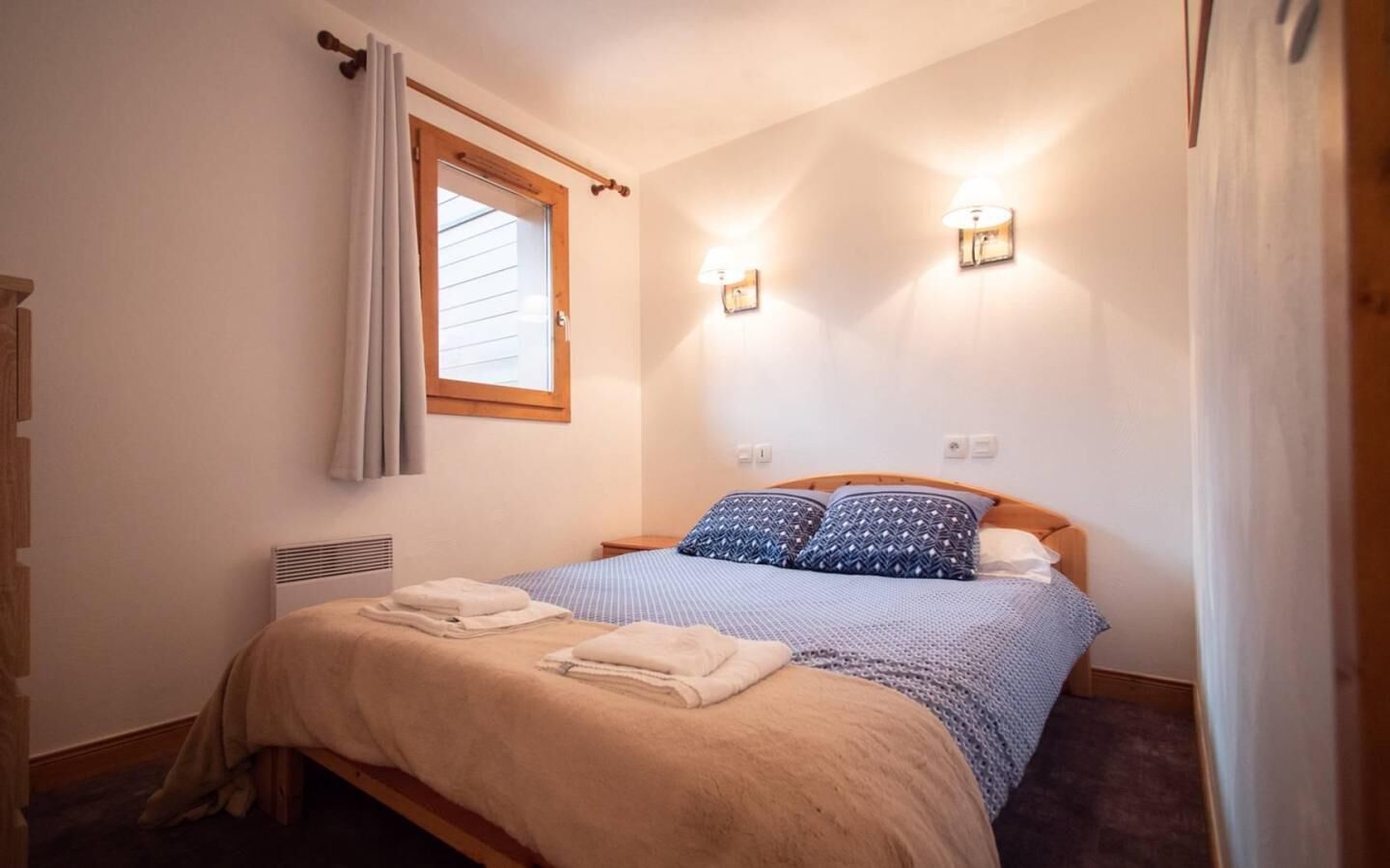 Ein Schlafzimmer mit einem Bett, zwei Wandleuchten, einem fenster mit Vorhängen und einer Heizung.