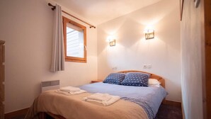 Un dormitorio con cama, dos lámparas de pared, una ventana con cortinas y un radiador.