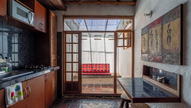 Une cuisine avec des meubles en bois, un plan de travail noir et un pare-feu en carrelage. Une fenêtre offre une vue sur un banc rouge situé à l’extérieur.