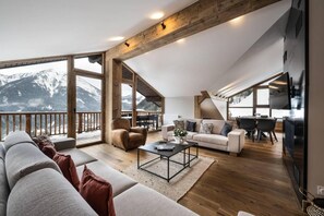 Un vaste espace de vie avec une grande fenêtre donnant sur une montagne enneigée, un canapé confortable, une table basse et un coin repas avec vue.