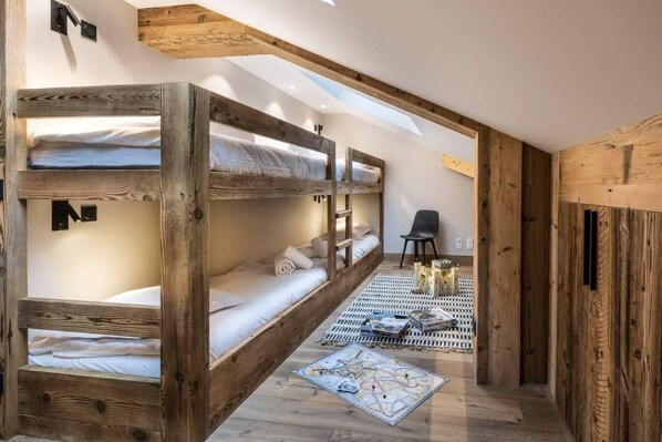 Une chambre avec un lit superposé, des poutres en bois, une petite table avec un jeu de société et une chaise.