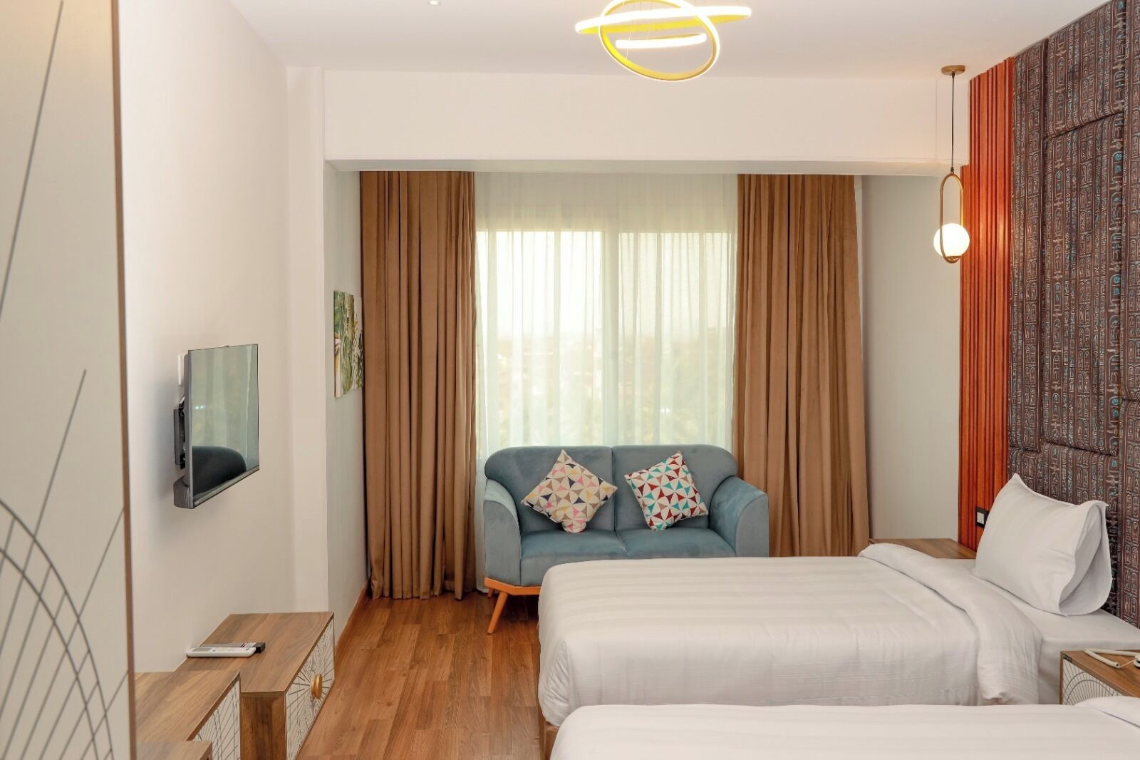 A hotel room with a bed, a sofa, a TV, and a window with curtains.