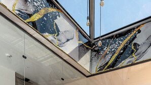 Un intérieur moderne avec deux fauteuils confortables, un sol en marbre poli et une cloison en verre qui reflète des œuvres d’art.