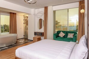 A modern hotel room with a large bed, a bathtub, a green sofa, and a large window offering a city view. -  La Veranda Pyramids Boutique Hotel (Giza)