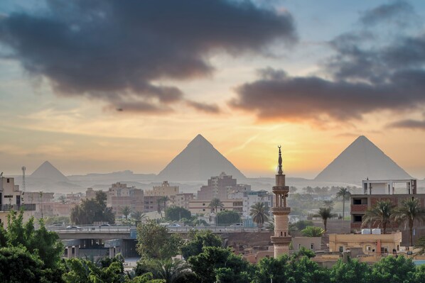 A cityscape with two prominent pyramids in the background, modern buildings, and a mosque with a minaret. -  La Veranda Pyramids Boutique Hotel (Giza)