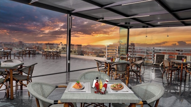 Un espace de restauration aménagé sur le toit, avec des tables et des chaises, offrant une vue sur la ville et un magnifique coucher de soleil.
