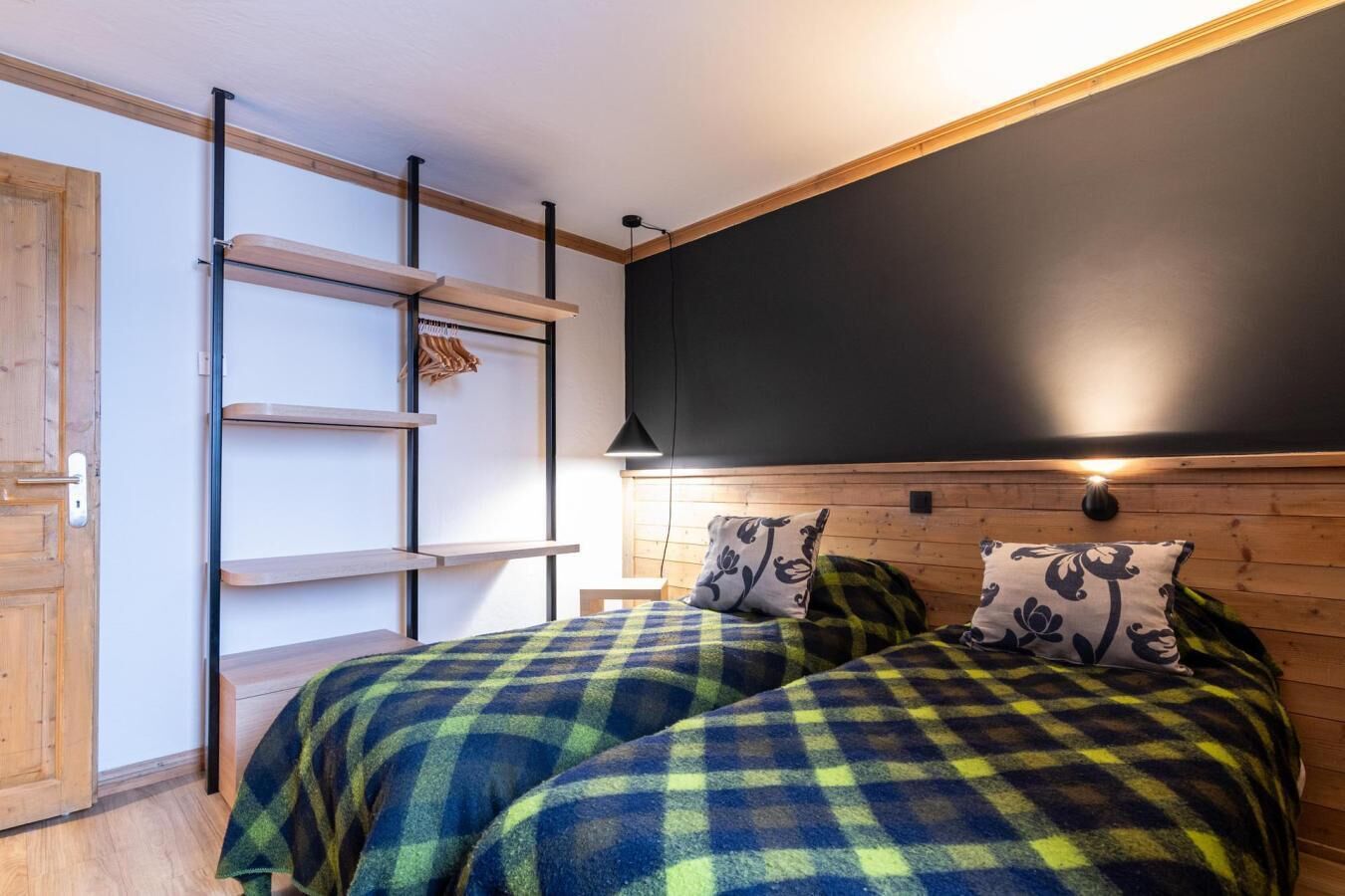 Une chambre avec deux lits, une tête de lit en bois, des étagères et une porte.