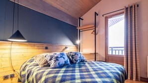 Une chambre à coucher avec une couvre-lit à carreaux, une tête de lit en bois et une fenêtre avec des rideaux.