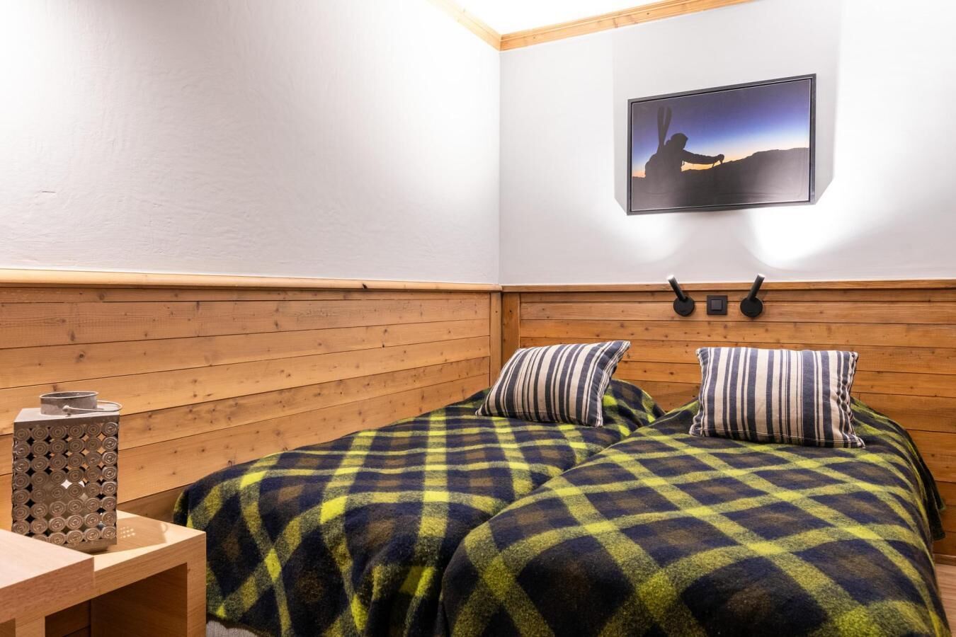 A room with a wooden headboard, two beds with striped pillows, a wall-mounted picture, and a small table with a decorative item.