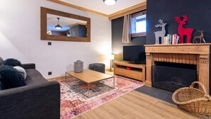 A living room with a sofa, a coffee table, a TV, a fireplace, and a mirror. - 100m from ski slopes, 1st floor, balcony, fireplace or stove, tv, ski locker, 66m², Val Thorens (Val Thorens)