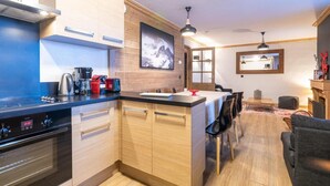 A modern kitchen with wooden cabinets, a built-in stove, and a dining area with a table and chairs. - 100m from ski slopes, 1st floor, balcony, fireplace or stove, tv, ski locker, 66m², Val Thorens (Val Thorens)