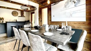 A modern dining area with a wooden ceiling, a large painting, and a dining table set for six with white chairs. - 300m from resort center, 1st floor, view mountain, terrace, fireplace or stove, tv, 140m² (Champagny-en-Vanoise)