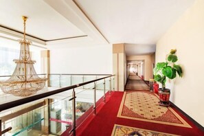 A hotel corridor with a red carpet, a chandelier, and a potted plant. - City 118 Chain Hotel Zhengzhou Economic Development Zone (Zhengzhou)