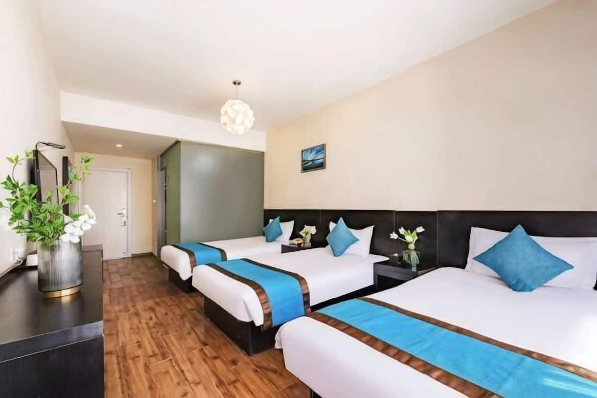 Habitación de hotel con tres camas, un escritorio, un florero con flores y un cuadro en la pared.