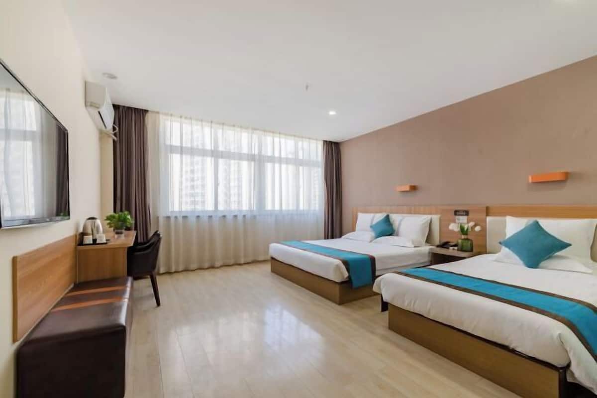 Habitación de hotel con dos camas, un escritorio, una silla y un ventanal grande con cortinas.