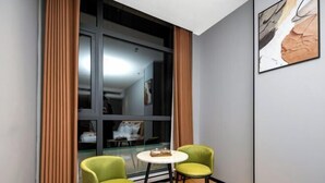 A corner room with a glass partition, two green chairs, a small round table, and a framed picture on the wall. - City 118 Chain Hotel Zhengzhou Economic Development Zone (Zhengzhou)