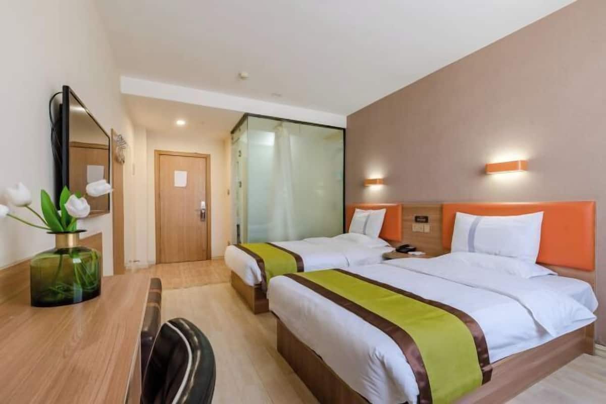 Habitación de hotel con dos camas, un escritorio, una silla, un espejo y un jarrón con flores.