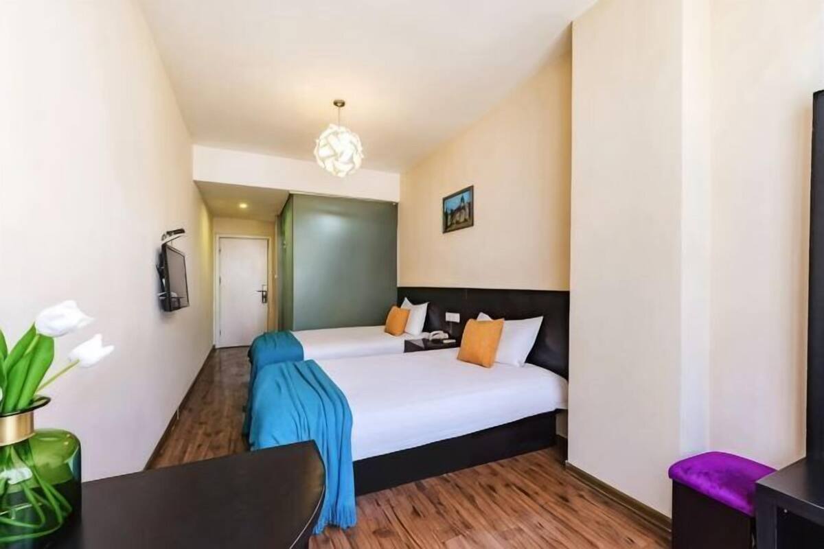 Habitación de hotel con dos camas, un escritorio, una silla, un televisor y una puerta que da a otra habitación.