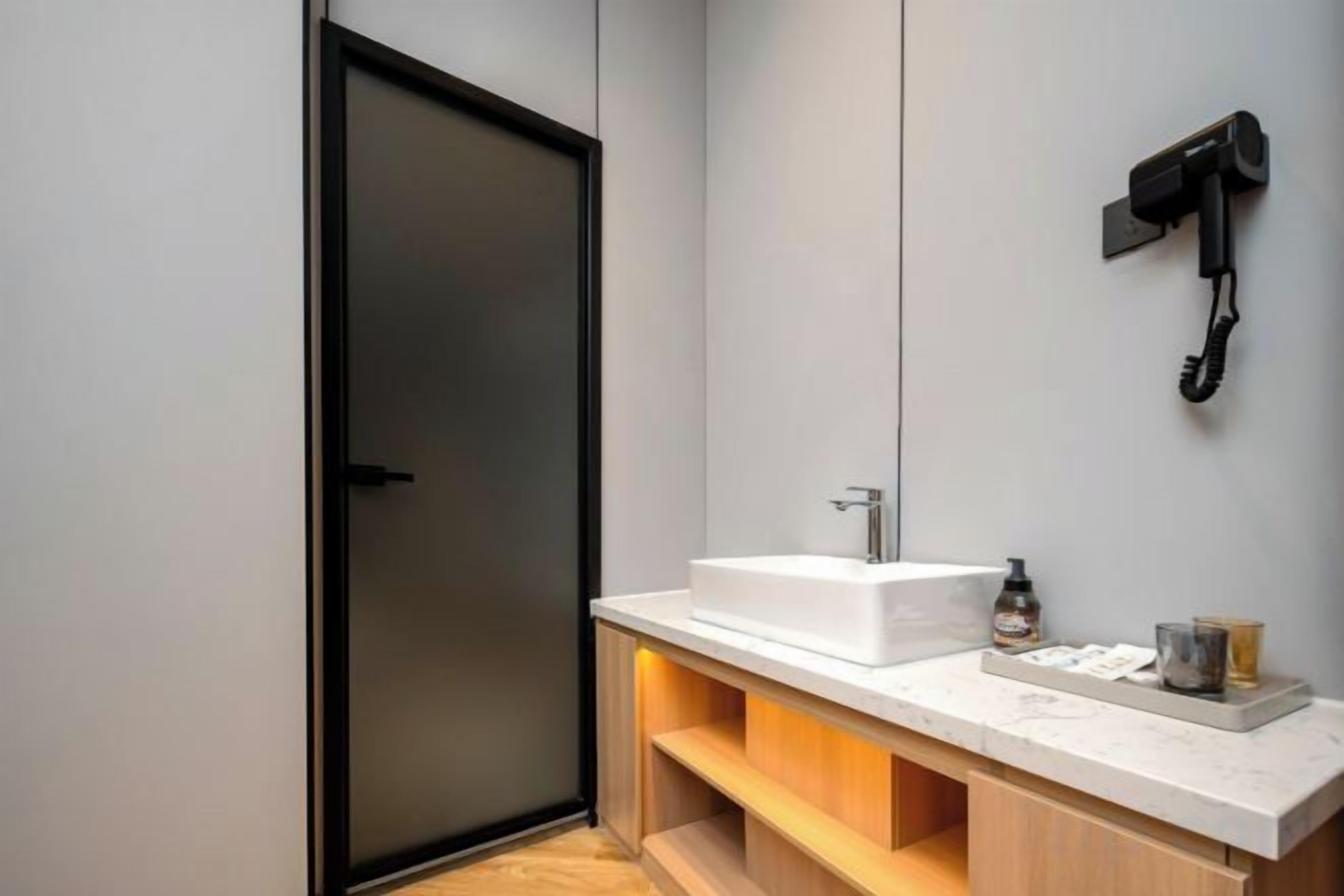 Een moderne badkamer met een grote spiegel, een witte wastafel en een aan de muur bevestigde haardroger.