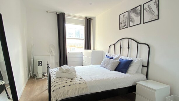 Une chambre à coucher avec un lit, des tables de chevet, un radiateur et une fenêtre avec des rideaux.
