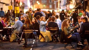 Une rue animée où l’on voit des gens assis à des tables, probablement dans un café en plein air.