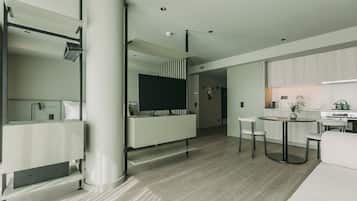 Uma sala de estar moderna com sofá, mesa de centro e televisão. Há uma área de cozinha com armários e fogão.