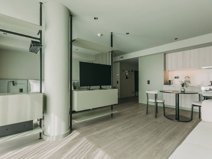 Uma sala de estar moderna com sofá, mesa de centro e televisão. Há uma área de cozinha com armários e fogão.