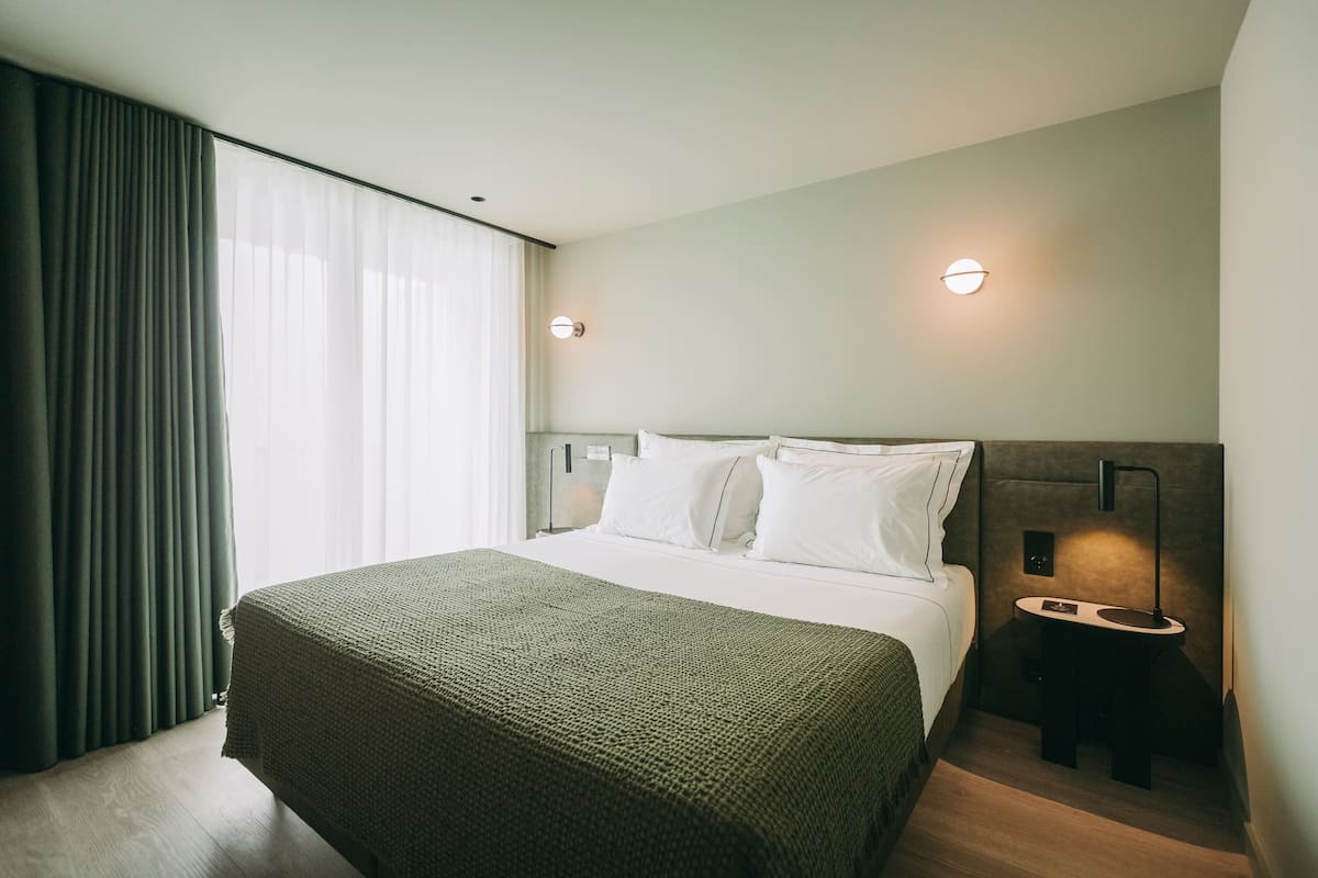 A modern hotel room with a large bed, a bedside table, and a nightstand.