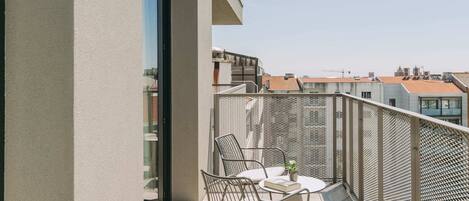 Un balcón con mesa y sillas, una barandilla de metal y vistas a edificios.