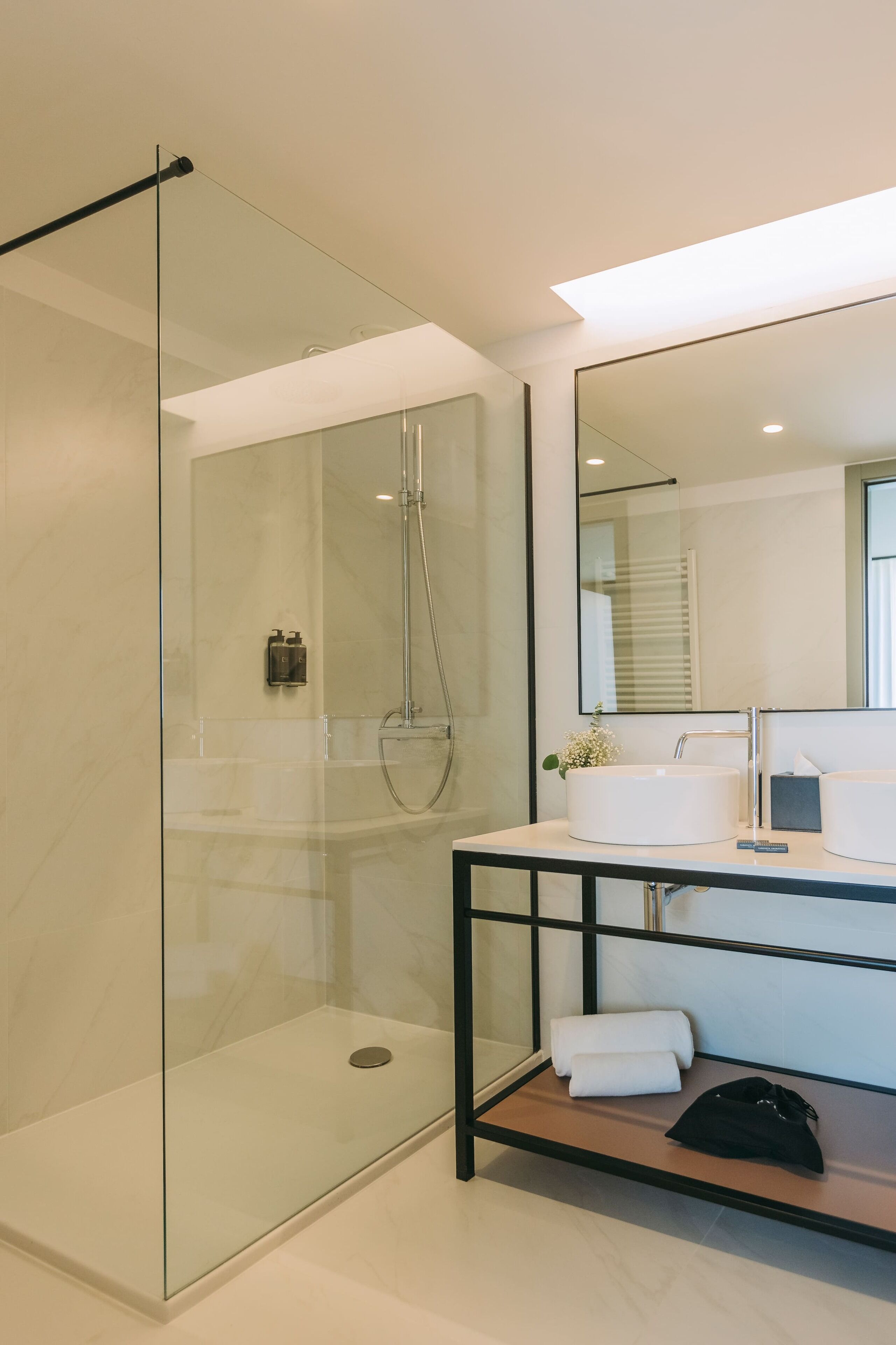 A modern bathroom with a glass-enclosed shower, a large mirror, and a vanity with a sink and towel rack.