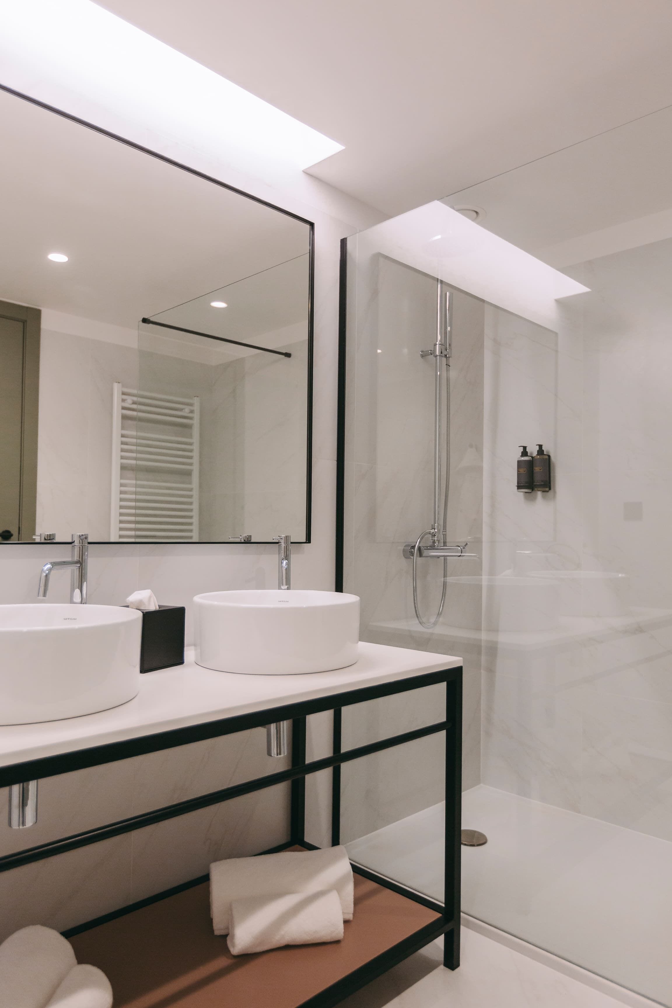 A modern bathroom with two sinks, a large mirror, and a glass-enclosed shower.