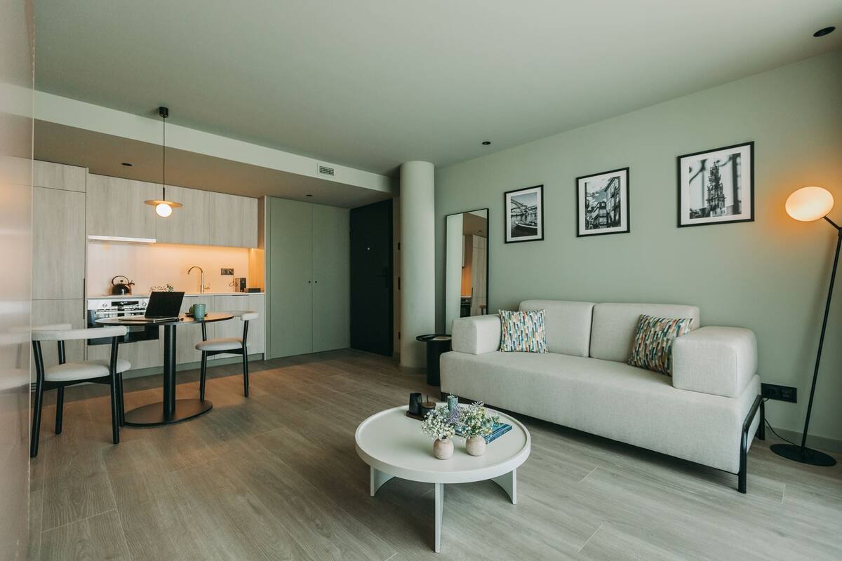 A modern apartment with a kitchen, dining area, and living room. It includes a white sofa, a coffee table, and framed pictures on the wall.