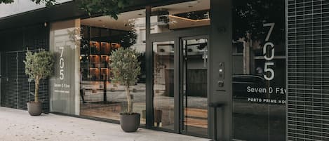 A modern building with a glass facade, large potted plants, and a sign reading "Seven O Five Porto Prime Home".