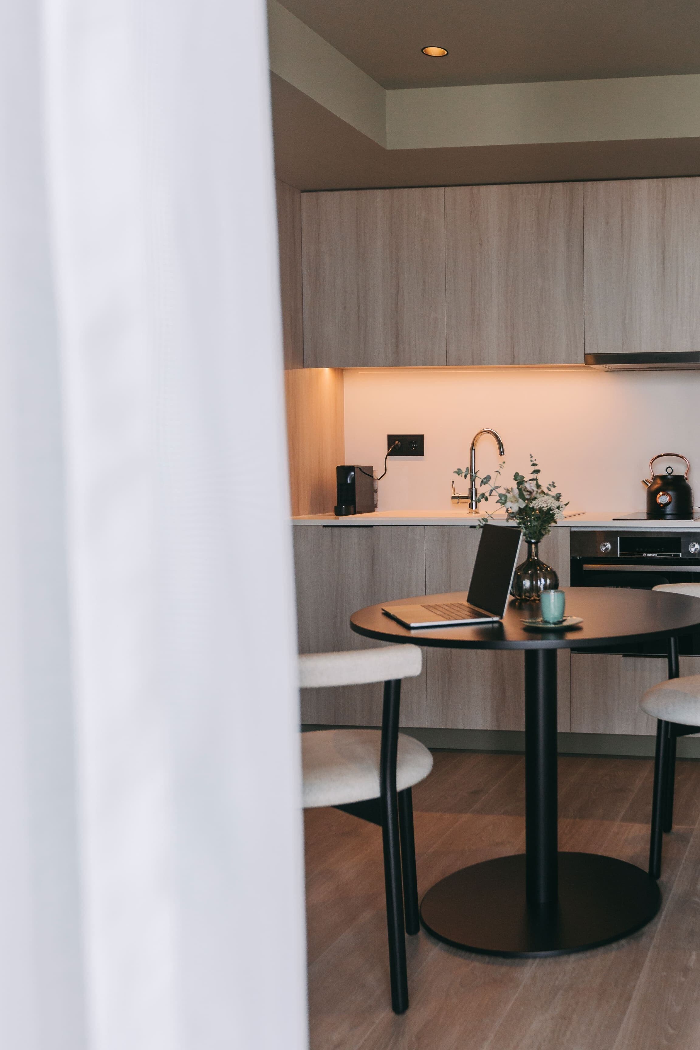 A modern kitchen with a round dining table, bar stools, and a kettle on the counter.