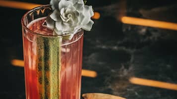 Un vaso alto con una decoración de rosa, una franja verde y una cuchara de madera con una sustancia verde a su lado.