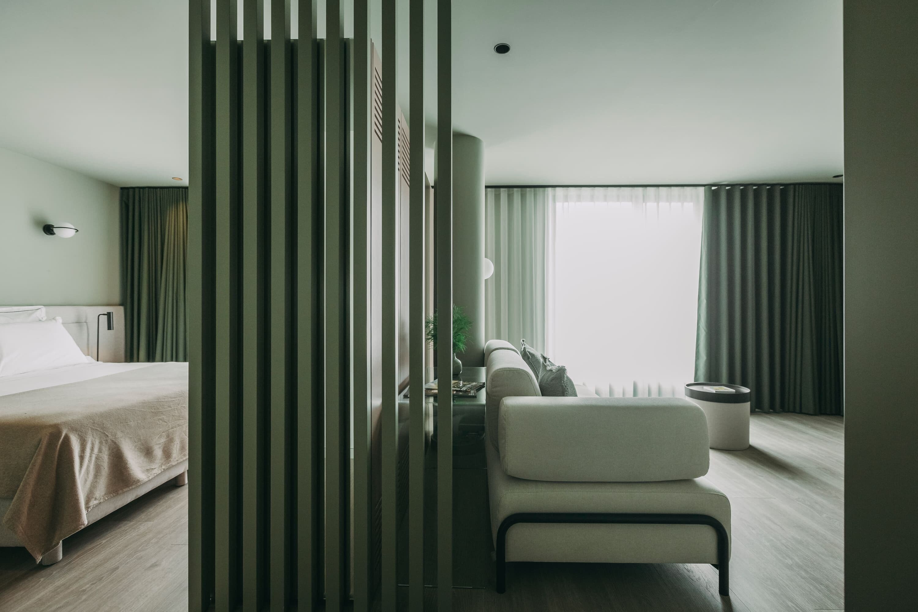 Habitación de hotel con cama, silla, escritorio, lámpara y ventana con cortinas.
