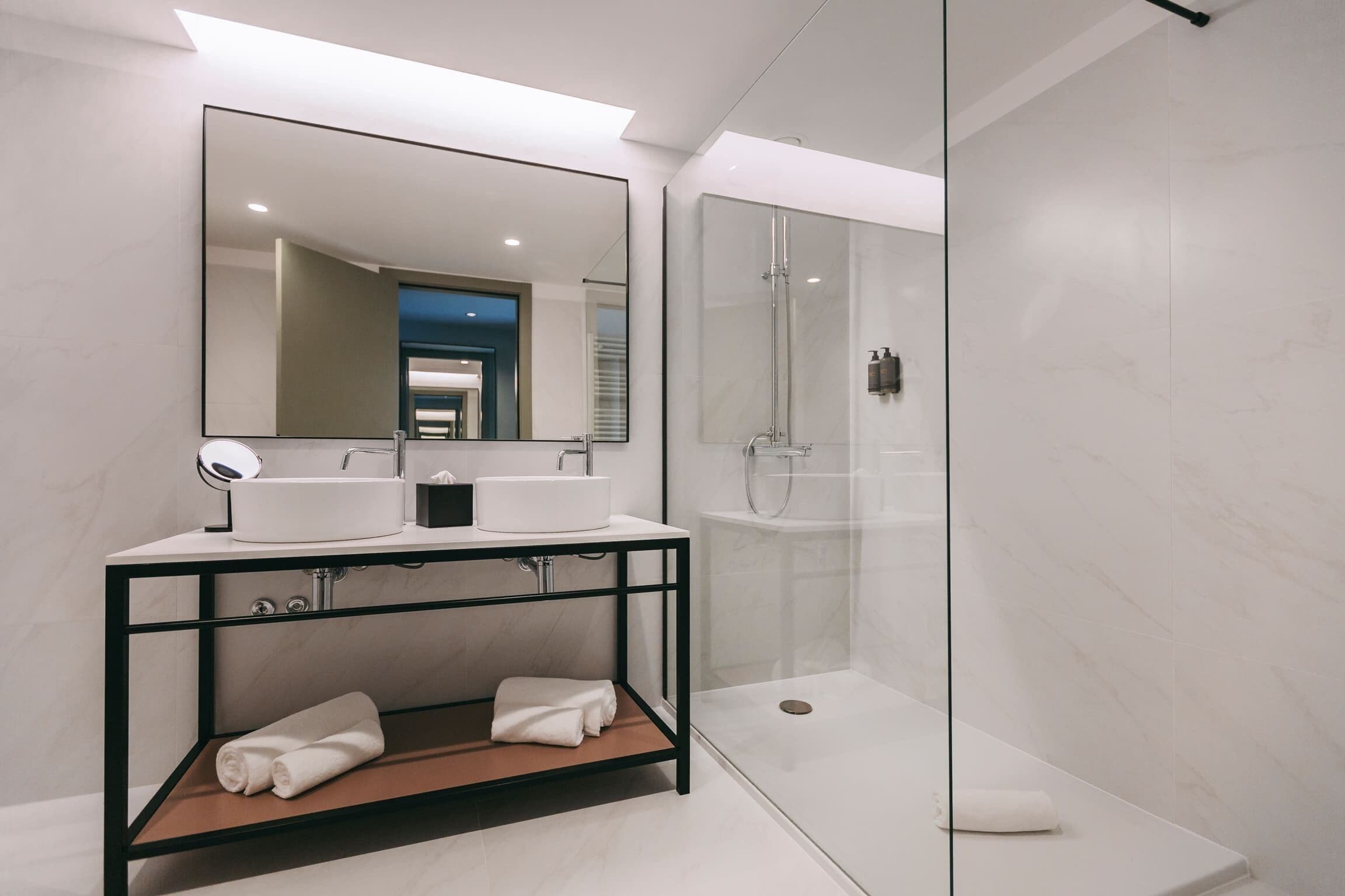 Un baño moderno con ducha acristalada, un espejo grande y un tocador doble.